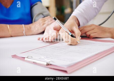 Close-up image of general practitioner talking to elderly woman and filling medical card Stock Photo