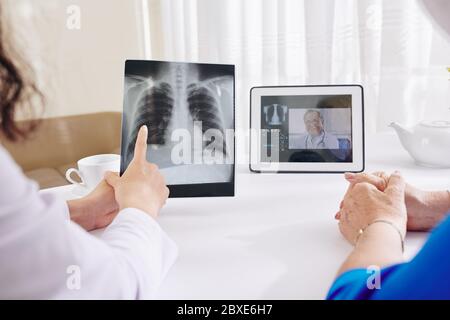 Pulmonologist checking lungs x-ray of senior woman and video calling senior colleague Stock Photo