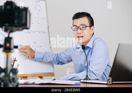 Young university teacher recording chemistry lesson on camera and explaining formula on whiteboard Stock Photo
