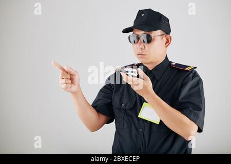 Serious policeman in sunglasses using walkie-talkie or police radio during demonstration and contolling work of officers