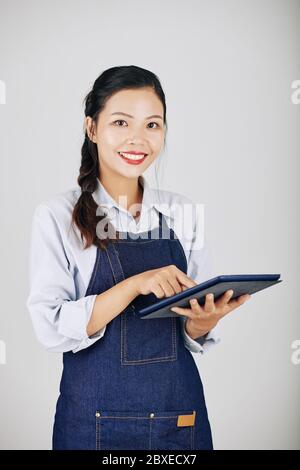 Portrait of smiling pretty Asian waitress using application on tablet computer when accepting order Stock Photo