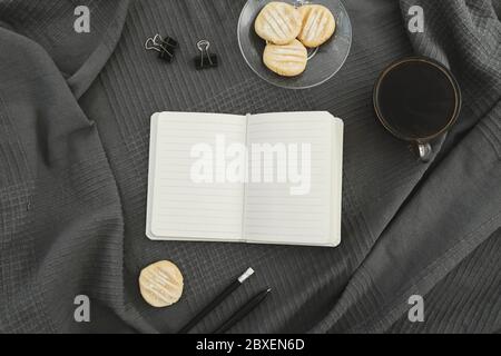 Freelancer concept. Coffee mug with cookies, diary and pen on gray plaid. Flat lay, top view. Stock Photo