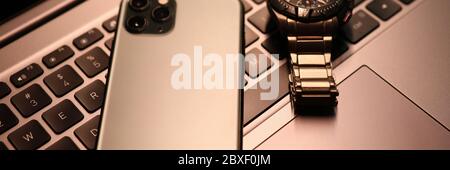 Silver smartphone and watch lie on laptop keyboard in office close-up Stock Photo