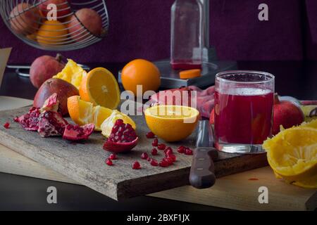 glass of freshly squeezed pomegranate juice, sliced fresh fruit into pieces, the process of squeezing juice Stock Photo