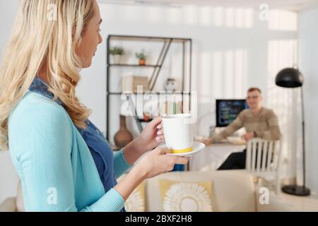 Young woman making cup of coffee for her husband who is working from home Stock Photo