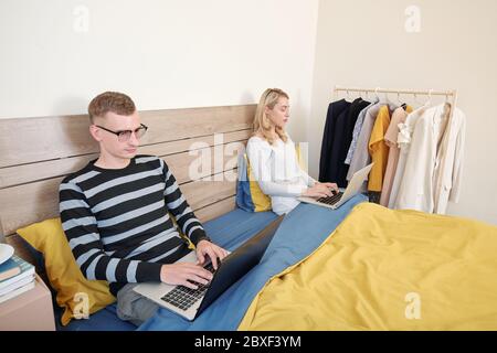Couple sitting on bed under blanket and working on laptops when social distancing at home during quarantine Stock Photo