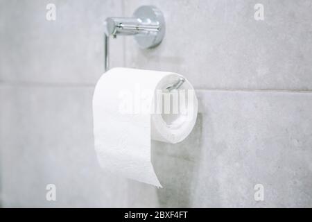 A roll of toilet paper hangs on a metal holder in the toilet or restroom. Stock Photo