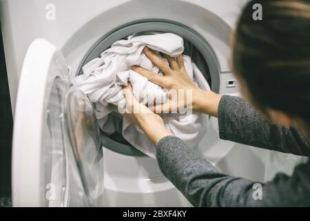 A woman or a housewife loads or puts the laundry in the dishwasher for washing. Stock Photo