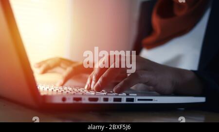 Close up hands typing on laptop in dark condition, writer work on computer, silhouette with sunset light from window Stock Photo
