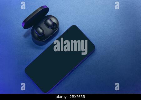 The wireless headphones in the box are unpacked and the cell phone on a classic blue background. Stock Photo