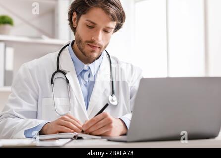 Doctor watching webinar on laptop and taking notes Stock Photo