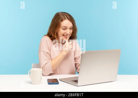 Please, keep secret. Positive young woman in casual clothes shushing with silence gesture, talking on video call, having online communication via lapt Stock Photo