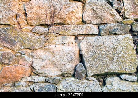 Stone wall texture made from uneven sized rocks with twigs and cobwebs in the gaps Stock Photo