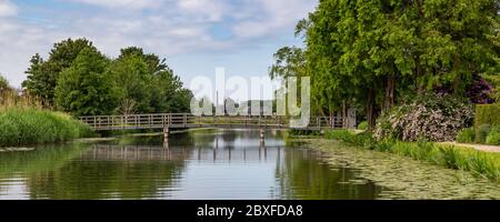 Natural large pond with bridge in a park surrouned by a meadows with colorful blooming plants, trees and grasses. Stock Photo
