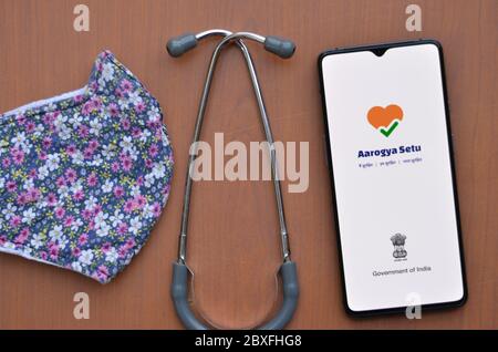 New Delhi, India, 2020. Flat lay with mobile showing Aarogya Setu app with stethoscope and designer floral face mask Wooden background. Concept Protec Stock Photo