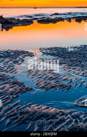 Ripples and reflections on wet beach sand in early morning light Stock Photo