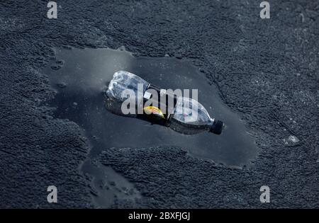 One empty , plastic, discarded soda bottle floating on pool of dark black water in the middle of black ice cover , Finland Stock Photo