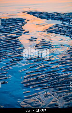 Ripples and reflections on wet beach sand in early morning light