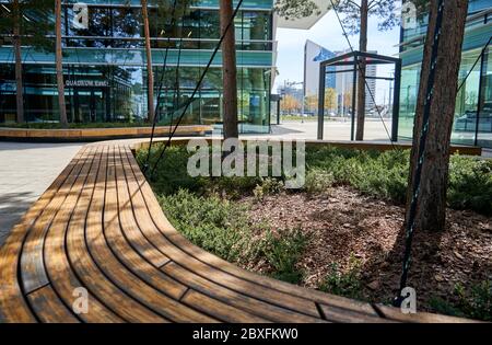 Wooden bench and some nature surrounded modern office buildings Stock Photo