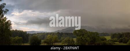 landscape with hills, forest and trees - rain, cloudy sky, partly shining blue sky Stock Photo