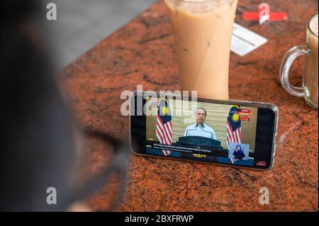 Kuala Lumpur, Malaysia. 7th June, 2020. A customer watches a televised speech by Malaysian Prime Minister Muhyiddin Yassin via mobile phone in Kuala Lumpur, Malaysia, June 7, 2020. Malaysia is further easing restrictive measures to allow nearly all social, education, commercial activities to resume since the latest figure suggests that the COVID-19 outbreak in the country is under control, Prime Minister Muhyiddin Yassin said on Sunday. Credit: Zhu Wei/Xinhua/Alamy Live News Stock Photo