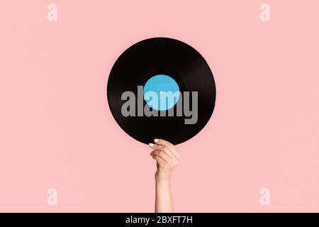 Girl hand showing retro vinyl gramophone record on pink background, closeup Stock Photo