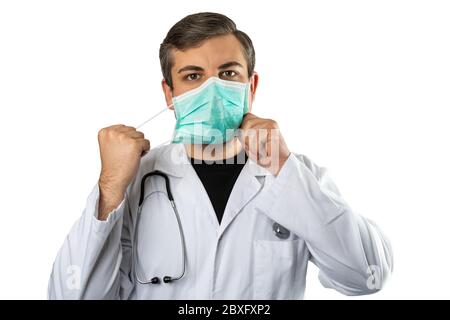 Caucasian man posing as a medical doctor in white overall or scrub with stethoscope around a neck taking off protective face mask. Isolated on white b Stock Photo