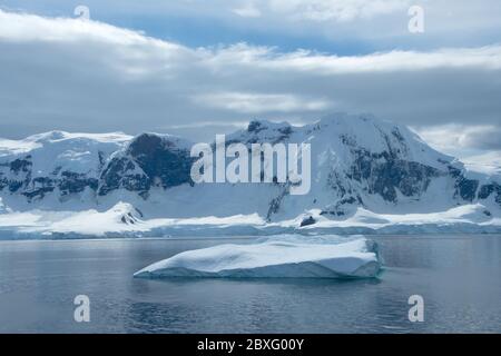 An iceberg floating in front of a snow covered Elephant Island, Antarctica.