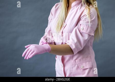 The doctor puts on pink protective gloves, close-up. Hands of a medic in a pink uniform. Preparing for medical procedure. Stock Photo