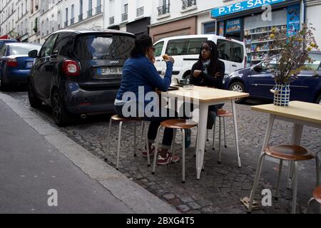 Parisians enjoy a temporary café terrace, between parked cars in life after lockdown - Rue Muller, Montmartre 75018 Paris, France Stock Photo