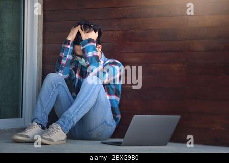Distressed man sitting on ground with his laptop during lockdown Stock Photo