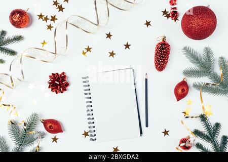 Christmas flat lay composition blank notebook among festive red decorations, golden confetti and green fir branches on white background. Stock Photo