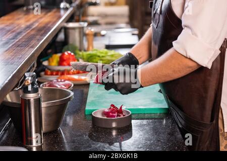 Close-up of unrecognizable chef in apron using knife while peeling red onion at commercial kitchen Stock Photo