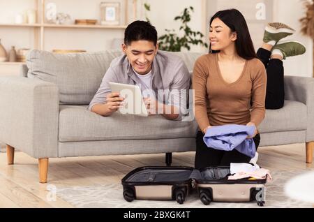 Happy Couple Using Tablet Computer Packing Sitting With Suitcase Indoor