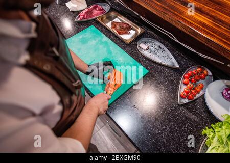 Above view of unrecognizable chef cutting fish on plastic board while preparing ingredients for dish Stock Photo
