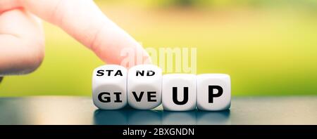 Hand turns dice and changes the expression 'give up' to 'stand up'. Stock Photo