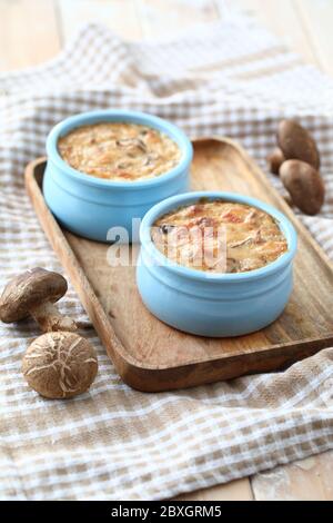 Mushroom gratins in two blue pots on a wooden tray Stock Photo