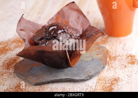 Chocolate muffin in a baking paper on a rustic table Stock Photo