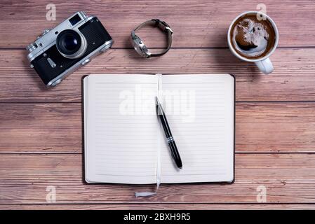 Vintage Travel camera and coffee cup with a planner notebook and wrist watch on an old wooden table. Top view Stock Photo