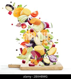 Vegetables falling onto wooden chopping board, isolated on white background Stock Photo