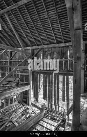Image is black and white.  interior of an old weathered barn.  View is from 2nd story.  There is an old fertilizer spreader inside. Stock Photo