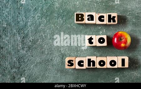 Back to school slogan on wooden cubes. Green blackboard background and ripe apple is a symbol of knowledge. Stock Photo