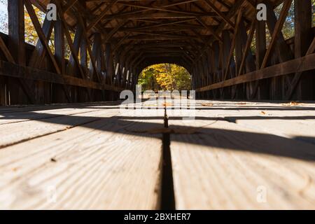 View along platform of Sunday River covered bridge with structure casting shadow pattern and leading lines. Sunday River, Maine, USA. Stock Photo