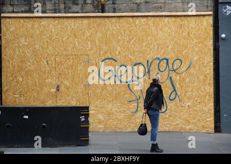Woman standing in the street looking at the name George Floyd written outside a boarded up shop in Edinburgh Scotland Stock Photo