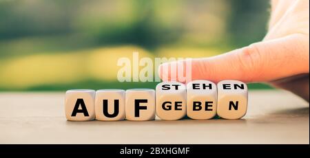 Hand turns dice and changes the German expression "aufgeben" ("give up") to "aufstehen" ("get up"). Stock Photo
