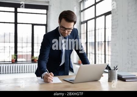 Serious businessman work on laptop making notes Stock Photo