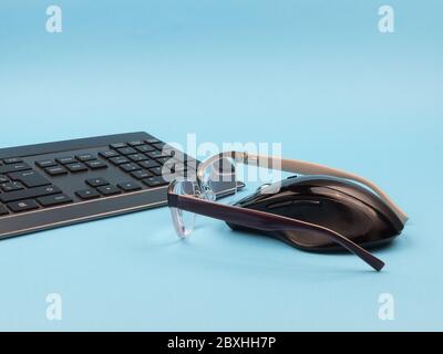 Keyboard, mouse and glasses on a blue background. Stock Photo