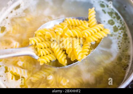 Pasta being cooked in a pan with boiler water and spatula checking for pasta Stock Photo