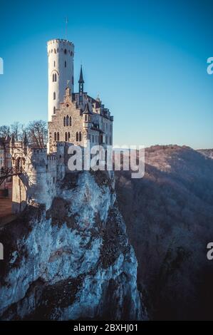 Castle standing on the rocky mountain in the rays of evening sun with a winter forest on the background under blue clear sky Stock Photo