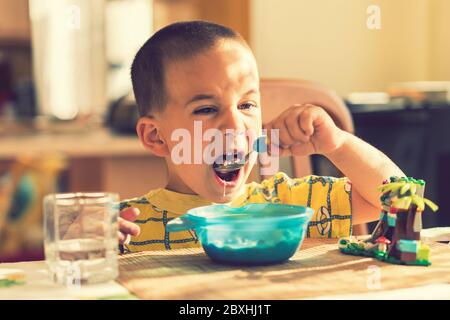 The boy 4 years eats porridge. Children's table. The concept of the child's independence. the boy is breakfasting with an appetite on the kitchen Stock Photo